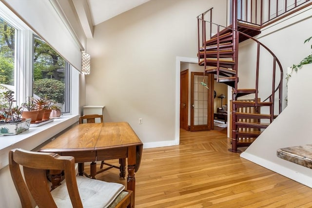 dining area with baseboards, high vaulted ceiling, stairs, and light wood-style floors