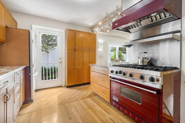 kitchen with stainless steel appliances, light wood-style floors, ventilation hood, and brown cabinetry