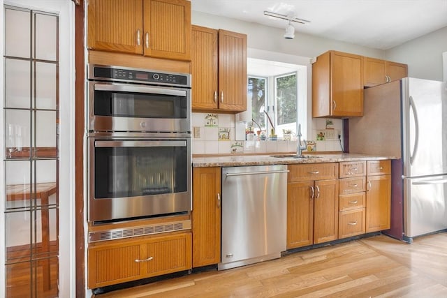 kitchen with stainless steel appliances, light wood finished floors, a sink, light stone counters, and brown cabinetry