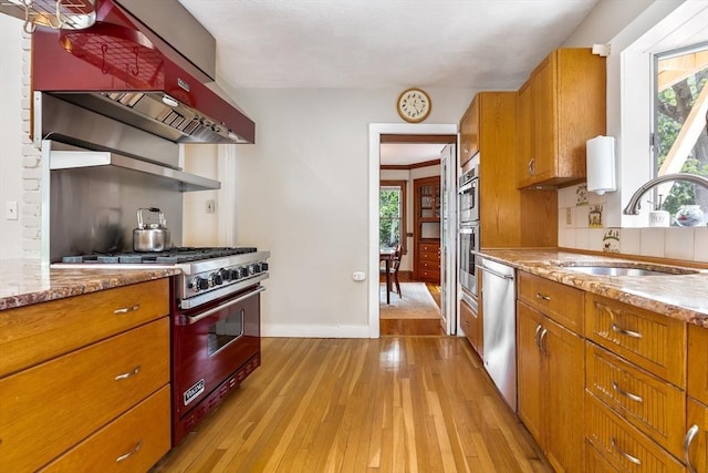 kitchen with appliances with stainless steel finishes, a sink, plenty of natural light, and brown cabinetry