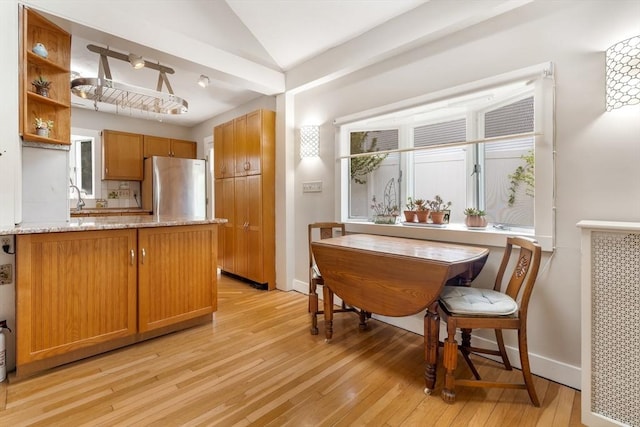 kitchen with freestanding refrigerator, light wood-style floors, lofted ceiling, baseboards, and light stone countertops