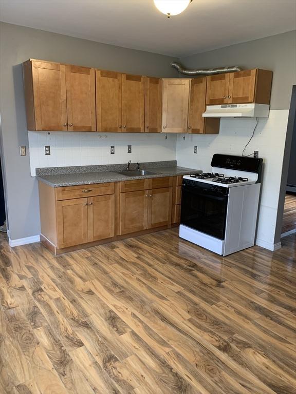 58 Ames Ave, Chicopee, MA 01013 - kitchen with gas stove, under cabinet range hood, dark wood-style floors, dark countertops, and baseboards