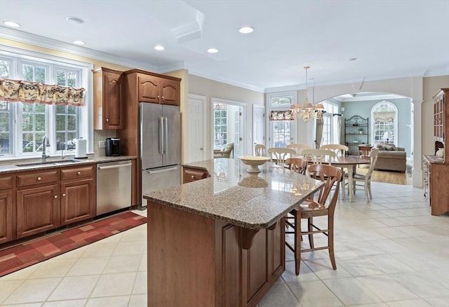 kitchen with ornate columns, appliances with stainless steel finishes, hanging light fixtures, a kitchen bar, and a kitchen island