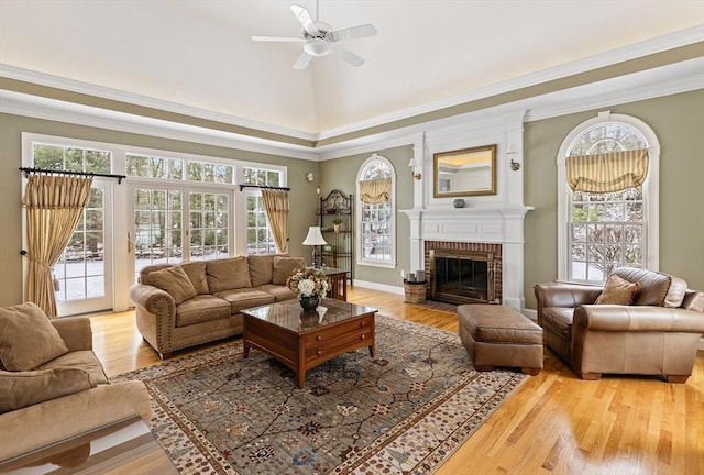 living room with vaulted ceiling, ornamental molding, ceiling fan, a fireplace, and light hardwood / wood-style flooring