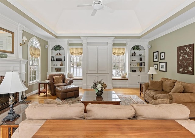 living room with ceiling fan, ornamental molding, a tray ceiling, and built in features