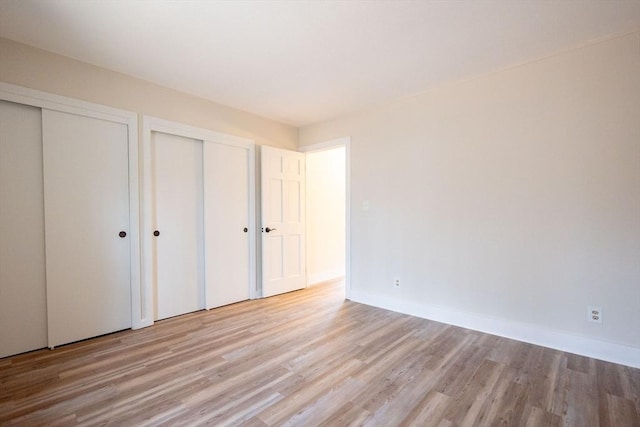 unfurnished bedroom featuring light hardwood / wood-style flooring and two closets