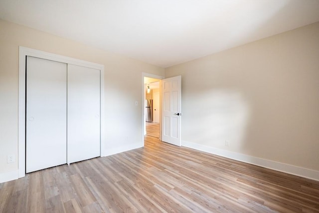 unfurnished bedroom with light wood-type flooring, a closet, and stainless steel refrigerator