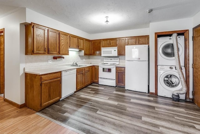 kitchen featuring sink, white appliances, hardwood / wood-style floors, stacked washer / dryer, and a textured ceiling