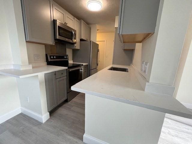 kitchen featuring kitchen peninsula, gray cabinetry, stainless steel appliances, sink, and wood-type flooring