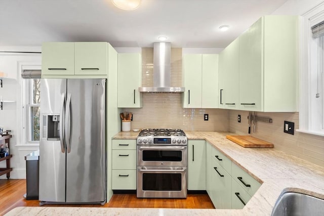 kitchen with green cabinetry, stainless steel appliances, wood finished floors, and wall chimney exhaust hood