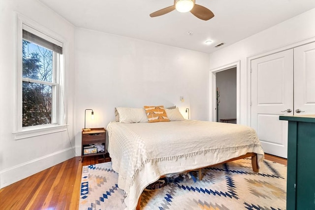 bedroom with visible vents, ceiling fan, baseboards, wood finished floors, and a closet