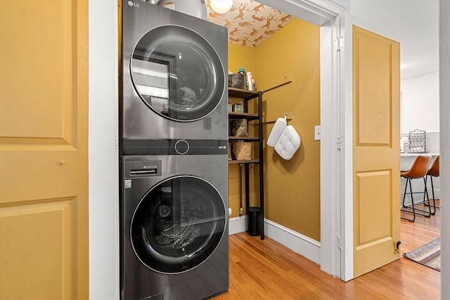 laundry area with laundry area, stacked washer and dryer, wood finished floors, and baseboards