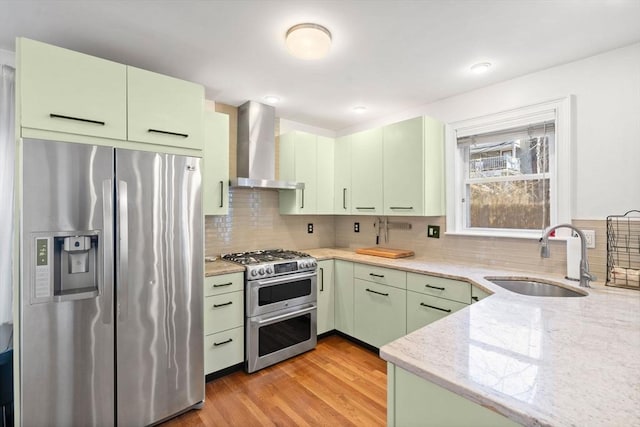 kitchen featuring wall chimney range hood, green cabinetry, and stainless steel appliances