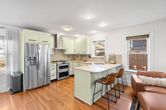 kitchen with a sink, stainless steel appliances, a peninsula, a breakfast bar area, and wall chimney exhaust hood