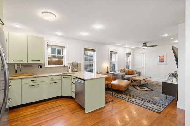 kitchen featuring a sink, stainless steel appliances, light wood-style floors, a peninsula, and green cabinets