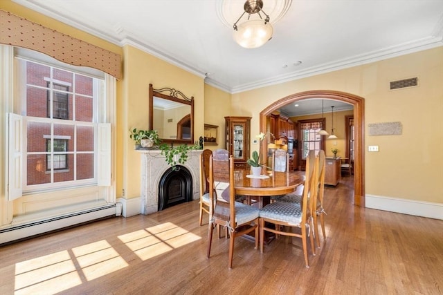 dining space with baseboards, visible vents, arched walkways, ornamental molding, and wood finished floors