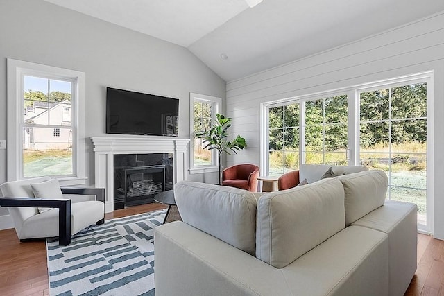 living room featuring wood walls, lofted ceiling, a tile fireplace, hardwood / wood-style flooring, and a wealth of natural light