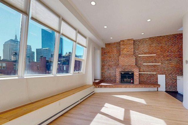 unfurnished living room with a baseboard radiator, a city view, brick wall, a fireplace, and light wood-style floors