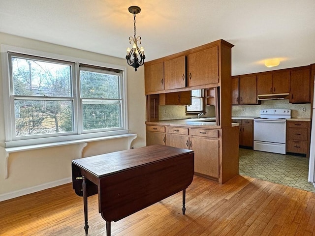 kitchen featuring under cabinet range hood, decorative light fixtures, decorative backsplash, light wood-style flooring, and electric stove