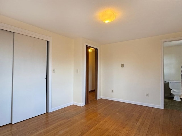 unfurnished bedroom featuring ensuite bathroom, baseboards, light wood-type flooring, and a closet