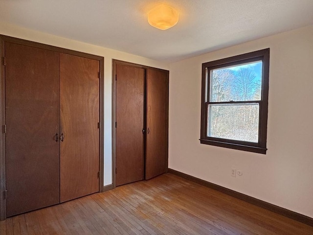 unfurnished bedroom featuring baseboards, two closets, and light wood finished floors