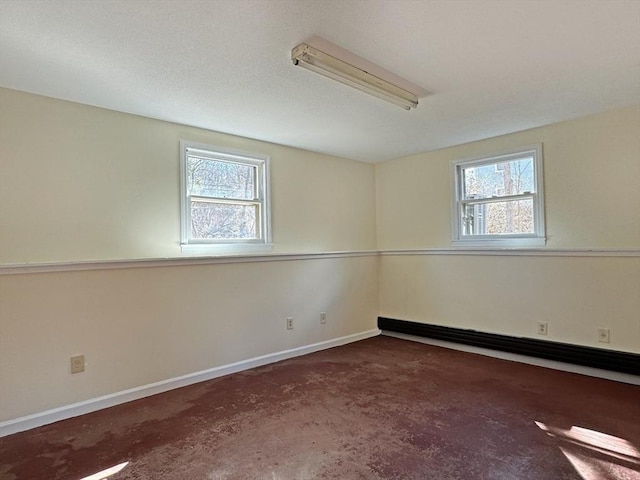 unfurnished room with a baseboard heating unit, plenty of natural light, and baseboards