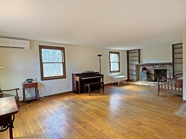 living area with plenty of natural light, hardwood / wood-style flooring, a fireplace with raised hearth, and a wall unit AC