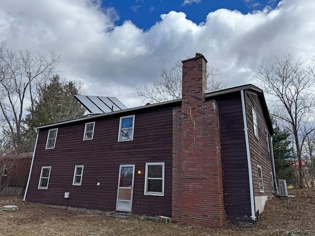 back of house with central AC unit and a chimney