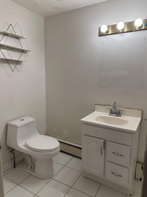 bathroom featuring a textured ceiling, tile patterned flooring, toilet, a baseboard heating unit, and vanity