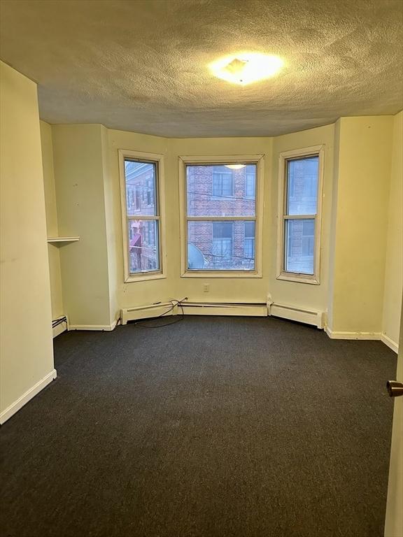 empty room with a textured ceiling, a baseboard radiator, and dark carpet