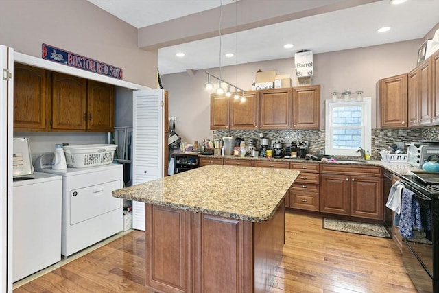 kitchen with light stone counters, black range with electric cooktop, light wood-style floors, and washer and clothes dryer