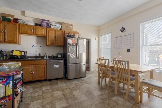 kitchen with brown cabinetry, a sink, stainless steel appliances, dark countertops, and tasteful backsplash