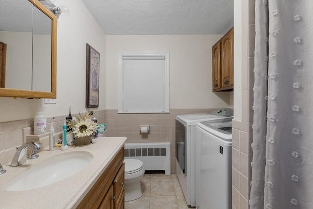 interior space featuring radiator, laundry area, a sink, tile walls, and washer and clothes dryer