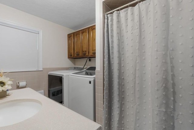 laundry room with a sink, a textured ceiling, separate washer and dryer, tile walls, and laundry area