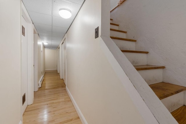 hallway with light wood finished floors, baseboards, stairway, a paneled ceiling, and a baseboard radiator