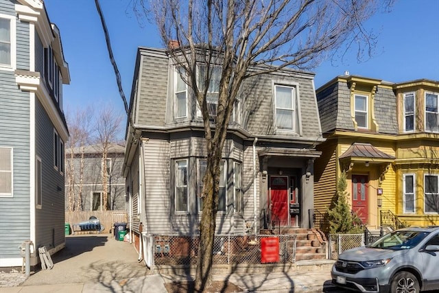 view of front of property featuring mansard roof, a fenced front yard, and a shingled roof