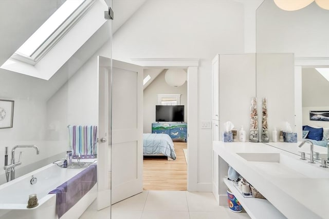 bathroom featuring a bath, tile patterned flooring, vanity, lofted ceiling with skylight, and ensuite bath
