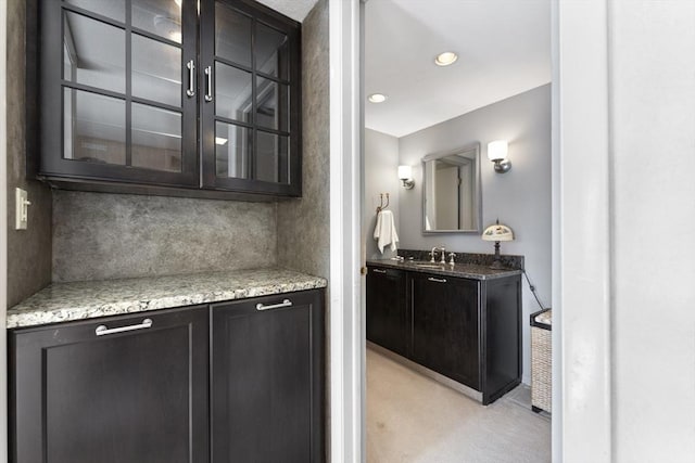 bar featuring backsplash, light stone countertops, and sink