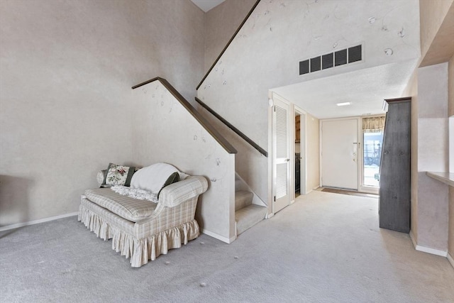 interior space featuring carpet flooring, a towering ceiling, visible vents, stairs, and baseboards