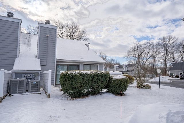 view of snowy exterior featuring a chimney and central AC unit