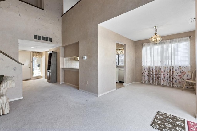 interior space with an inviting chandelier, a towering ceiling, and light colored carpet