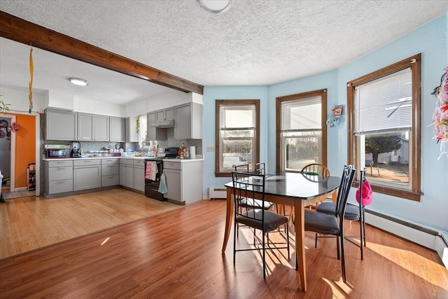 dining space with beam ceiling, a textured ceiling, a baseboard heating unit, and light wood-type flooring