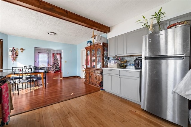 kitchen with beam ceiling, dark hardwood / wood-style floors, backsplash, stainless steel fridge, and gray cabinets