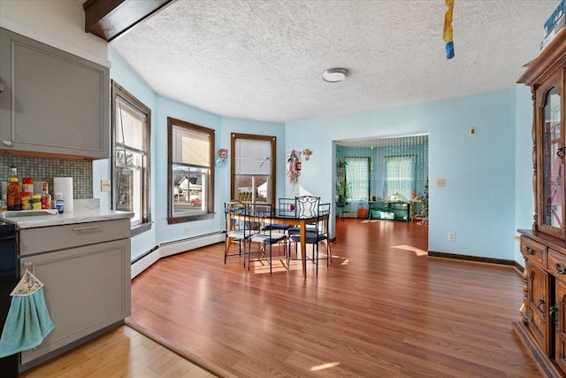 dining area featuring a textured ceiling, light hardwood / wood-style floors, plenty of natural light, and baseboard heating