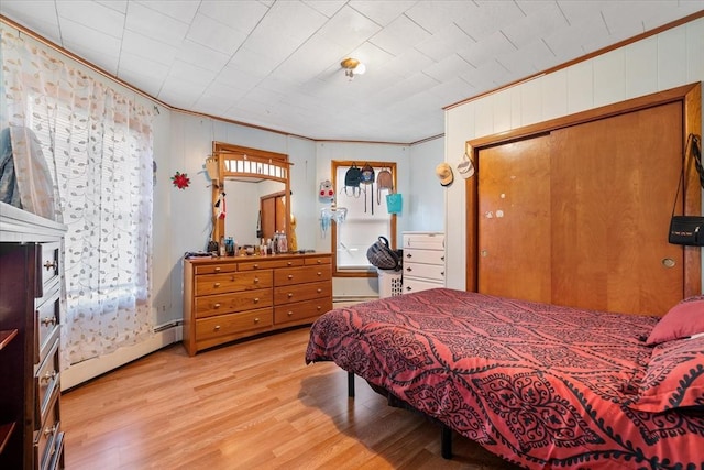 bedroom featuring light wood-type flooring, a baseboard radiator, a closet, and ornamental molding