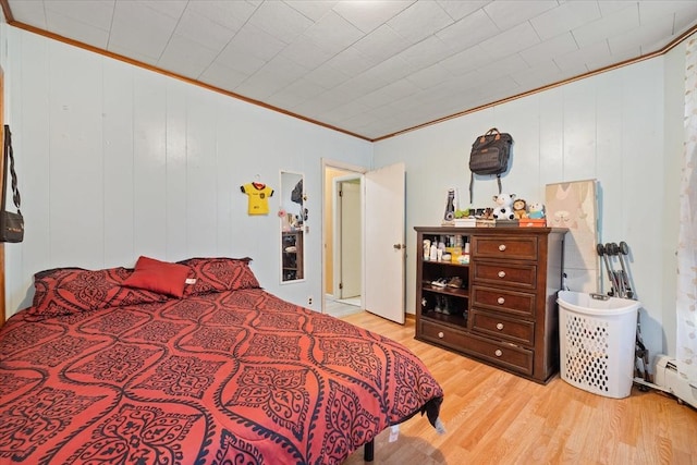 bedroom featuring a baseboard heating unit, light hardwood / wood-style flooring, crown molding, and wood walls