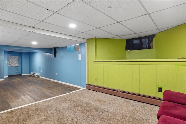 basement with a paneled ceiling, dark colored carpet, and a baseboard heating unit