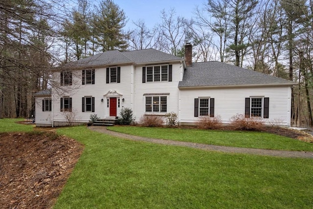 colonial-style house with a chimney, a front yard, and roof with shingles