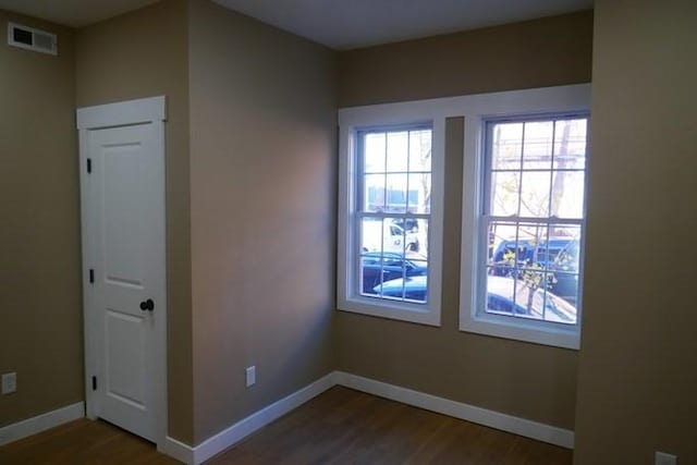 spare room with dark wood-style floors, visible vents, and baseboards