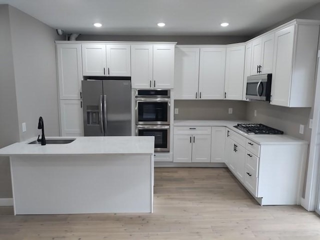 kitchen with stainless steel appliances, light countertops, white cabinetry, a sink, and light wood-type flooring